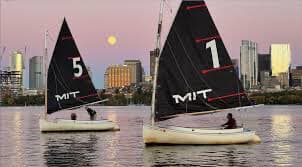 Two MIT sailboats with black sails on the Charles at dusk